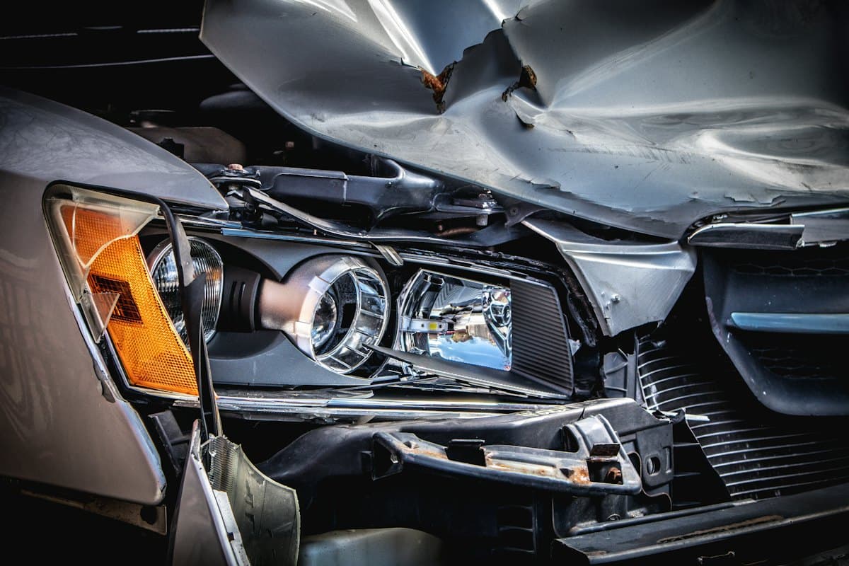 Frente de carro prata com capô amassado e farol danificado após uma colisão