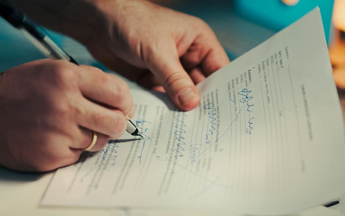 Mãos assinando um contrato de compra e venda de veículo com uma caneta