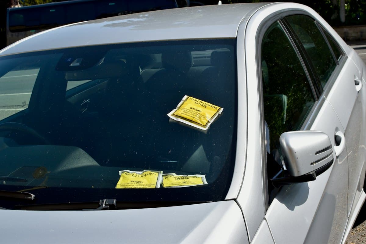 Carro prata com avisos de multa amarelos presos no para-brisa