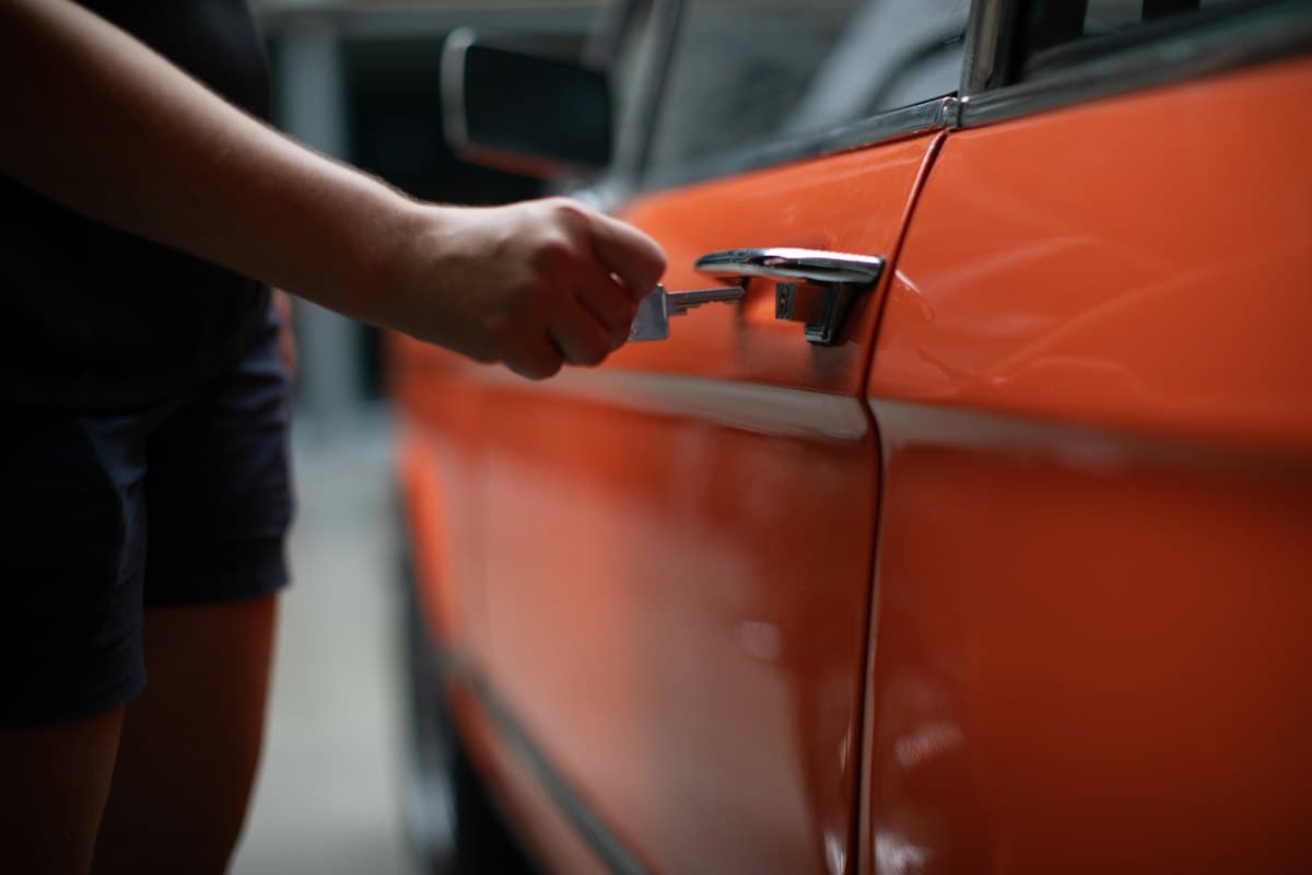 Mão com a chave abrindo a porta de um carro laranja